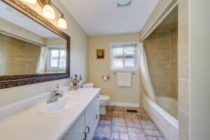Full bathroom with large vanity, framed mirror and tiled tub and shower combination.