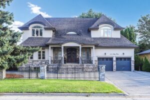 Front elevation of a luxury two-storey stone and stucco home with triple garage and landscaped front yard.
