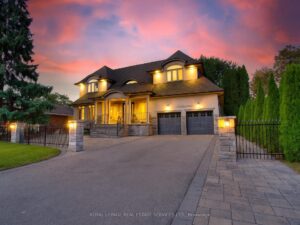 Evening exterior view of the home with illuminated architectural lighting and interlock driveway.
