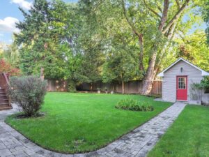Private backyard with mature trees, expansive lawn, garden shed, and stone walkway.