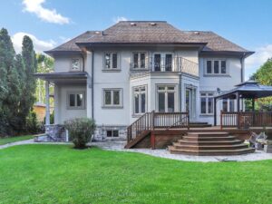 Rear exterior of the home with stone patio, landscaped lawn, and covered terrace.