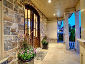 Covered front porch with stone columns, wood ceiling, and welcoming double-door entry.
