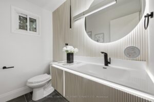 Modern main floor powder room with fluted vanity, backlit mirror, quartz countertop and contemporary black fixtures.