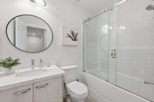 Modern full bathroom with quartz vanity, glass-enclosed bathtub and contemporary finishes.