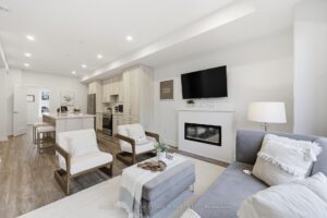 Open-concept living room featuring a modern fireplace, large windows and seamless connection to the kitchen.