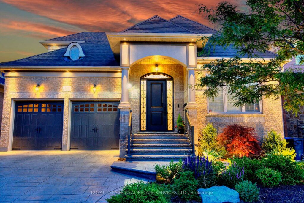 Twilight exterior of a luxury detached home with stone façade, landscaped gardens, and elegant architectural lighting.