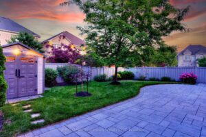 Twilight view of the private backyard with stone patio, mature landscaping, and garden shed.