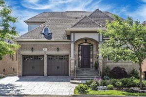 Front elevation of the home with double garage, interlock driveway, and mature landscaping.
