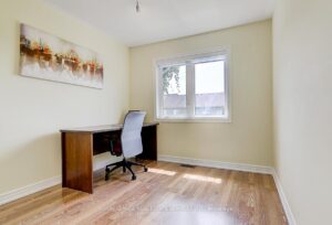 Bright bedroom or home office with hardwood flooring and large window.