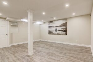 Finished basement recreation room with modern flooring, recessed lighting, and support columns.