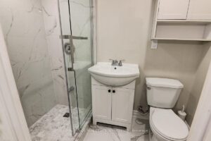 Modern basement bathroom with glass shower, marble-look tile, and pedestal vanity.