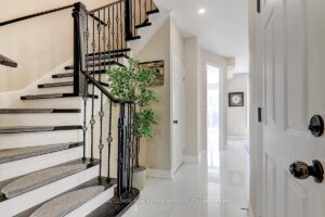Bright front foyer with tile flooring, hardwood staircase, and wrought-iron railings.