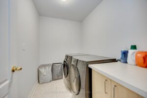Convenient upper-level laundry room at 2249 Glazebrook, Mississauga, with side-by-side washer, dryer, and storage cabinets.