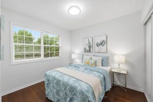 Bright bedroom with hardwood flooring, large picture window, and neutral finishes.