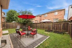 Fully fenced backyard with stone patio, outdoor dining area, and mature landscaping.