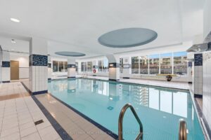 Indoor swimming pool with floor-to-ceiling windows and resident lounge area.