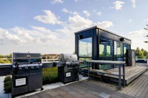 Rooftop BBQ station with outdoor grilling area and modern glass pavilion.