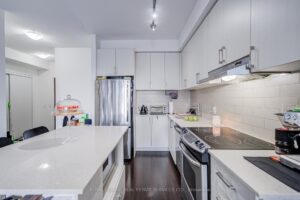 Modern galley kitchen with large centre island, white cabinetry, and stainless steel appliances.