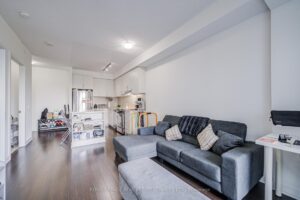 Open-concept living room with modern flooring, comfortable seating, and kitchen beyond.