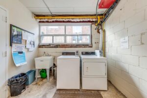 Shared laundry room with coin-operated washer, dryer and utility sink for resident convenience.
