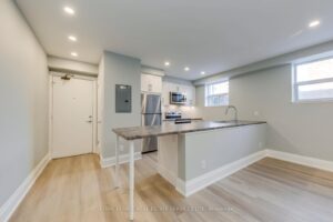 Renovated apartment kitchen with white cabinetry, stainless steel appliances, breakfast bar, and open layout.