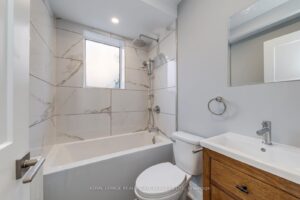 Modern bathroom with marble-look tile surround, rainfall shower, vanity, and contemporary fixtures.