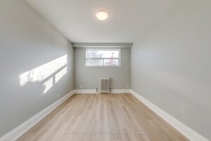 Bright bedroom with large window, neutral finishes, luxury vinyl flooring, and radiator heating.