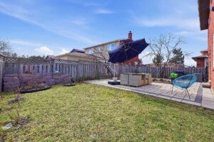 Fully fenced backyard with spacious lawn, stone patio, and mature trees.