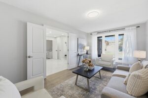 Bright living room with large windows, neutral décor, and double-door entry.