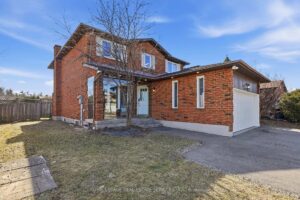 Side exterior of the brick detached home with yard and paved walkway.