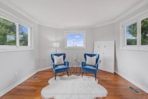 Primary bedroom sitting area with corner windows and blue accent chairs.