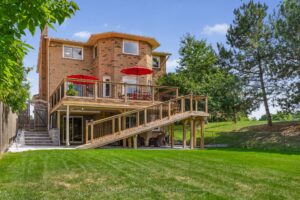 Rear exterior of the home with elevated deck, mature trees, and landscaped lawn.