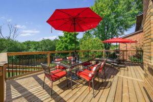 Spacious backyard deck with outdoor dining set, red umbrella, and treetop views.