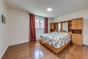 Bright secondary bedroom with hardwood flooring, large window, and built-in shelving.