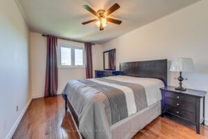 Spacious bedroom with hardwood flooring, ceiling fan, and contemporary furnishings.