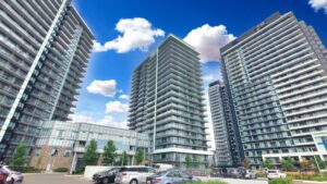 Exterior view of modern high-rise condominium towers with landscaped entrance and blue sky.