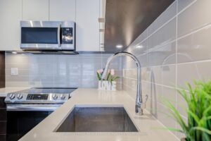 Kitchen sink area with quartz countertop, tile backsplash, and stainless steel range.