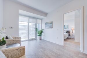 Bright living room with large window, light flooring, and bedroom doorway.