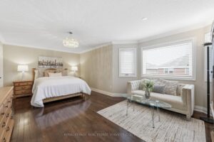 Primary bedroom featuring a comfortable sitting area, hardwood flooring, and abundant natural light.