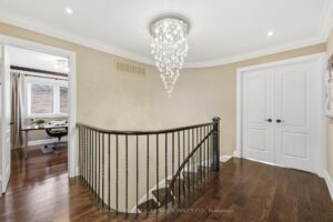 Second-floor landing with hardwood flooring, wrought-iron railings, and elegant chandelier.