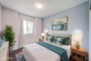 Comfortable bedroom with hardwood flooring, large window, and soft accent colours.