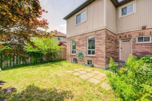 Fully fenced backyard with mature trees, lawn, and landscaped gardens.