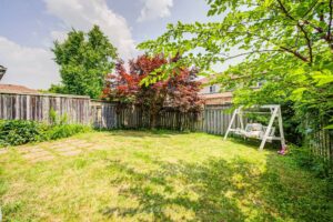 Spacious backyard with mature trees, swing set, and fully fenced lawn.