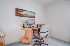 Flexible bedroom or home office with large window and neutral carpeting.