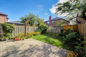 Fully fenced backyard with stone patio, mature gardens, and lawn area.