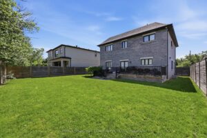 Fully fenced backyard with expansive lawn, mature trees, and neighbouring luxury homes.